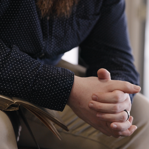A man is sitting with an open Bible, hands folded in prayer